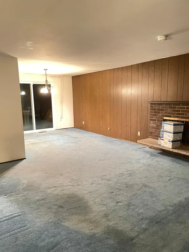 Living room before the remodel, with wood paneled walls and worn blue carpet