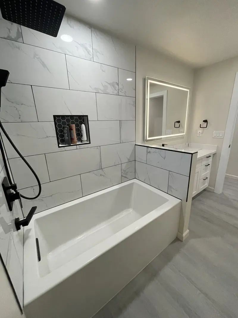 Soaking tub with a tiled niche, black fixtures and large-format marble-look tile