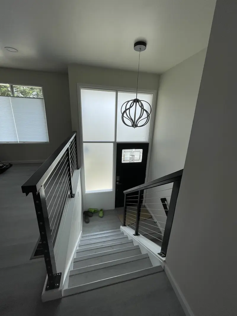 Stairs with a black cable railing and a round pendant light at the entry
