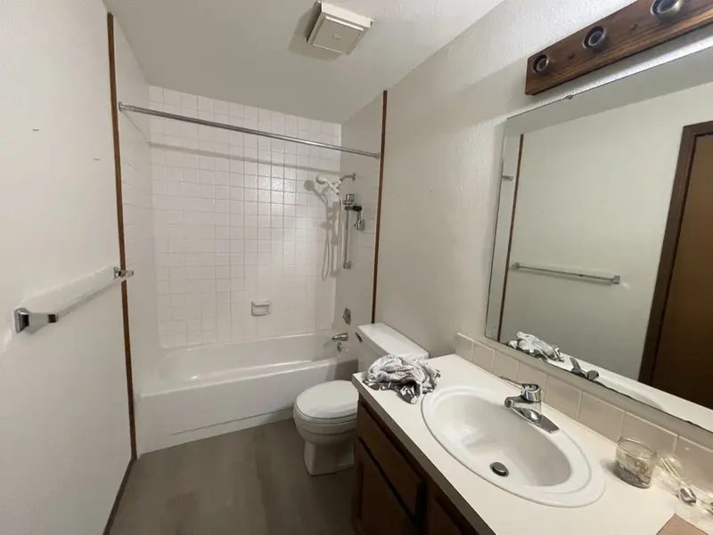 Older bathroom with a white tub surround, a cream vanity top and a vanity light bar