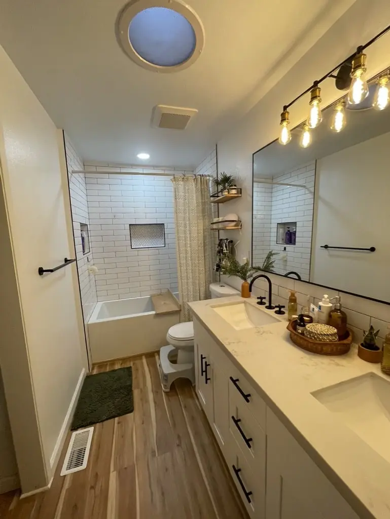 Bathroom with a white double vanity, black faucets, a skylight and a subway tile tub wall