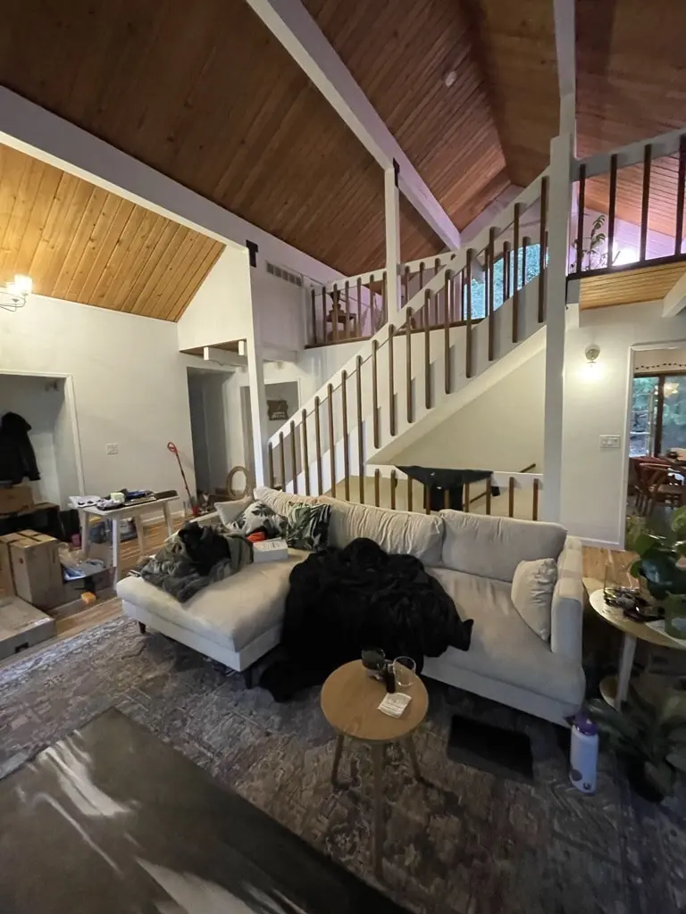 Great room with a vaulted wood ceiling, a white staircase railing and a sofa on the new floor
