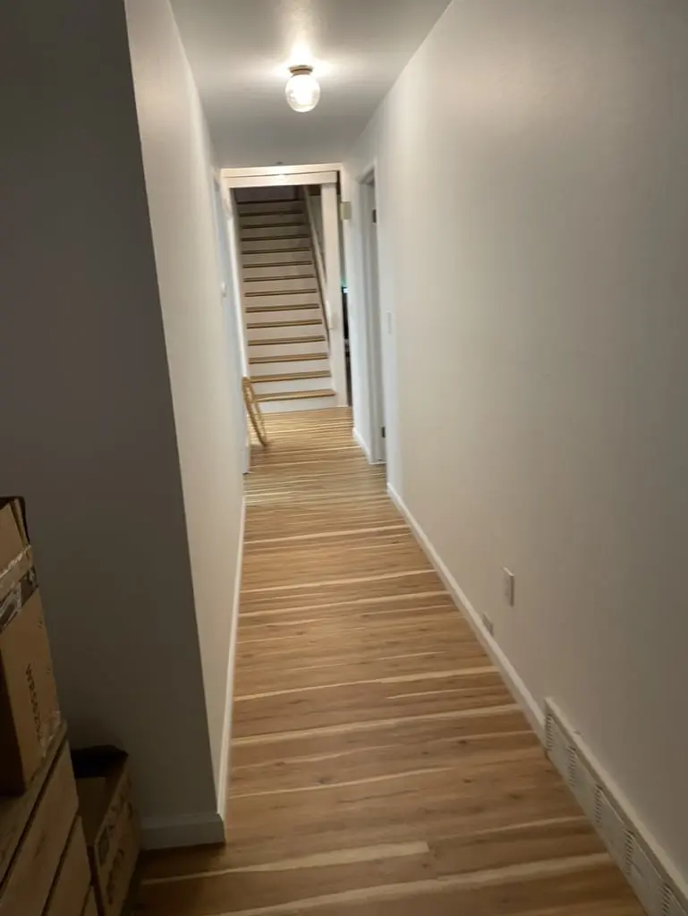 Long white hallway with a new wood floor leading to a staircase