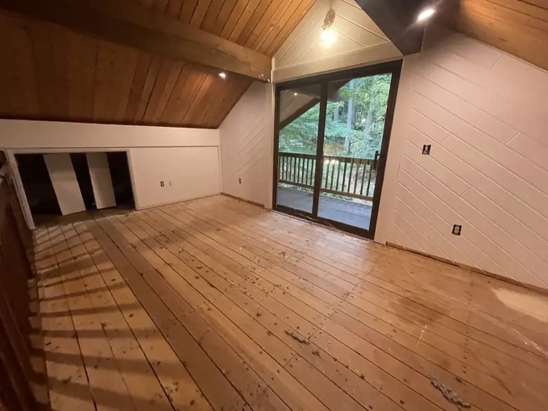 Upstairs room under a sloped wood ceiling with bare plank boards on the floor and a sliding door