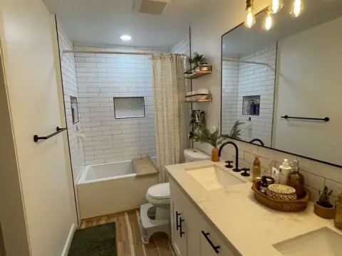 Remodeled bathroom in Redmond, WA with white subway tile, a tub with a niche, a double vanity and brass pendant lights