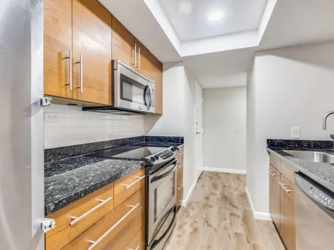 Condo kitchen with wood cabinets, dark granite counters and plank flooring in Renton, WA