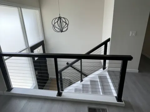 Stair landing with a black cable railing, gray plank flooring and a globe pendant light in a remodeled Renton, WA house
