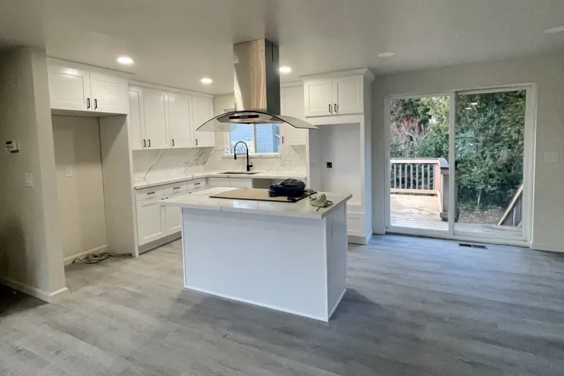 Open kitchen after a whole home remodel in Renton, WA with white shaker cabinets, a quartz island, a steel range hood and gray plank flooring