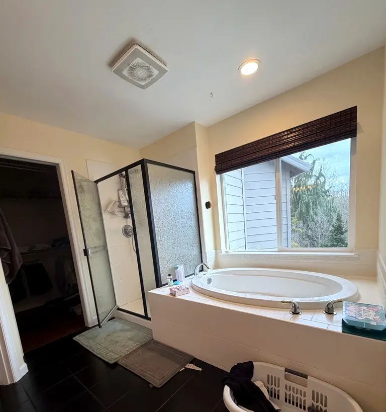 Old drop-in tub in a tiled deck under a window, next to a framed shower and a closet door