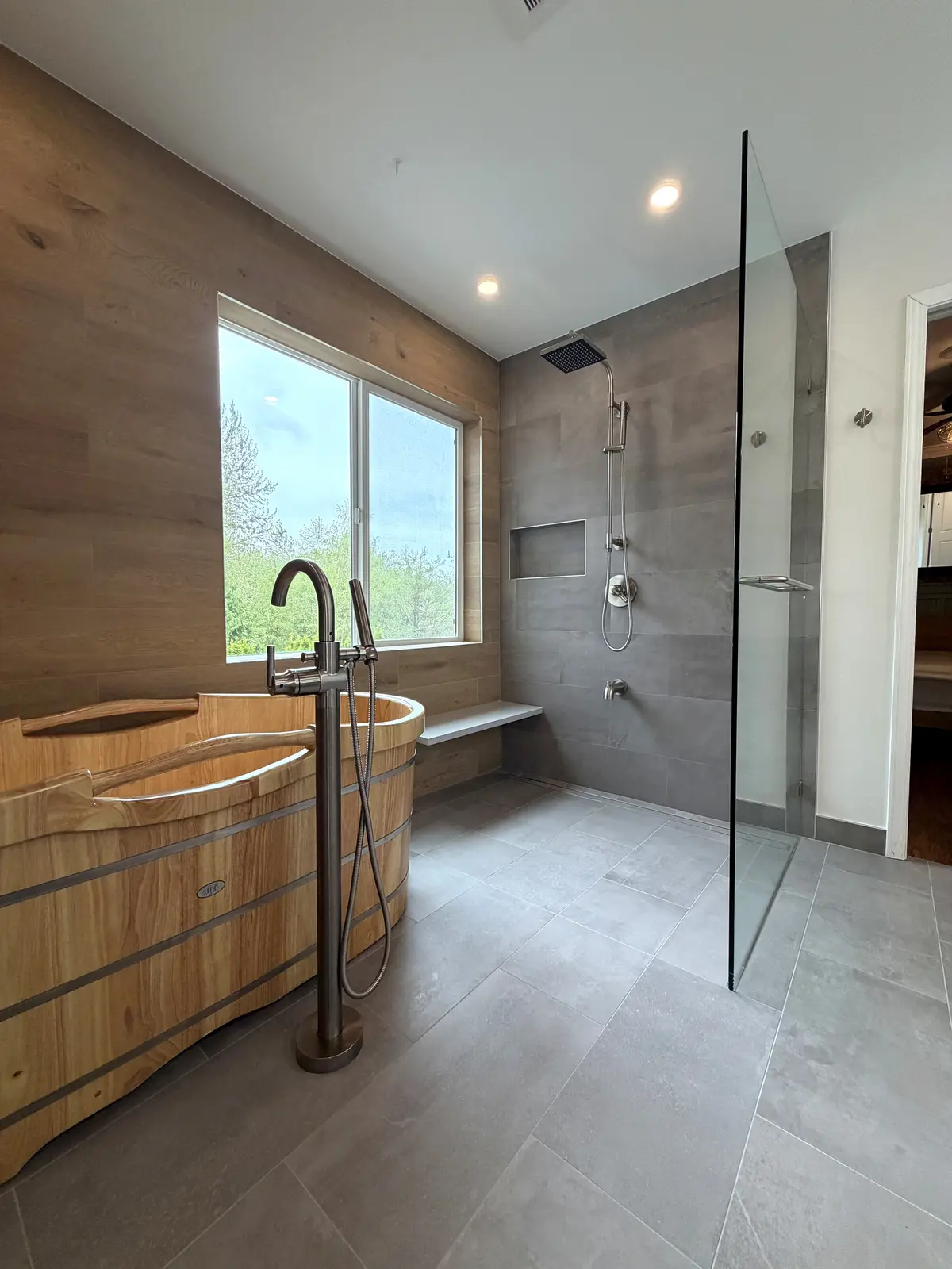 Wooden soaking tub with a floor-mounted filler by a window beside a walk-in shower