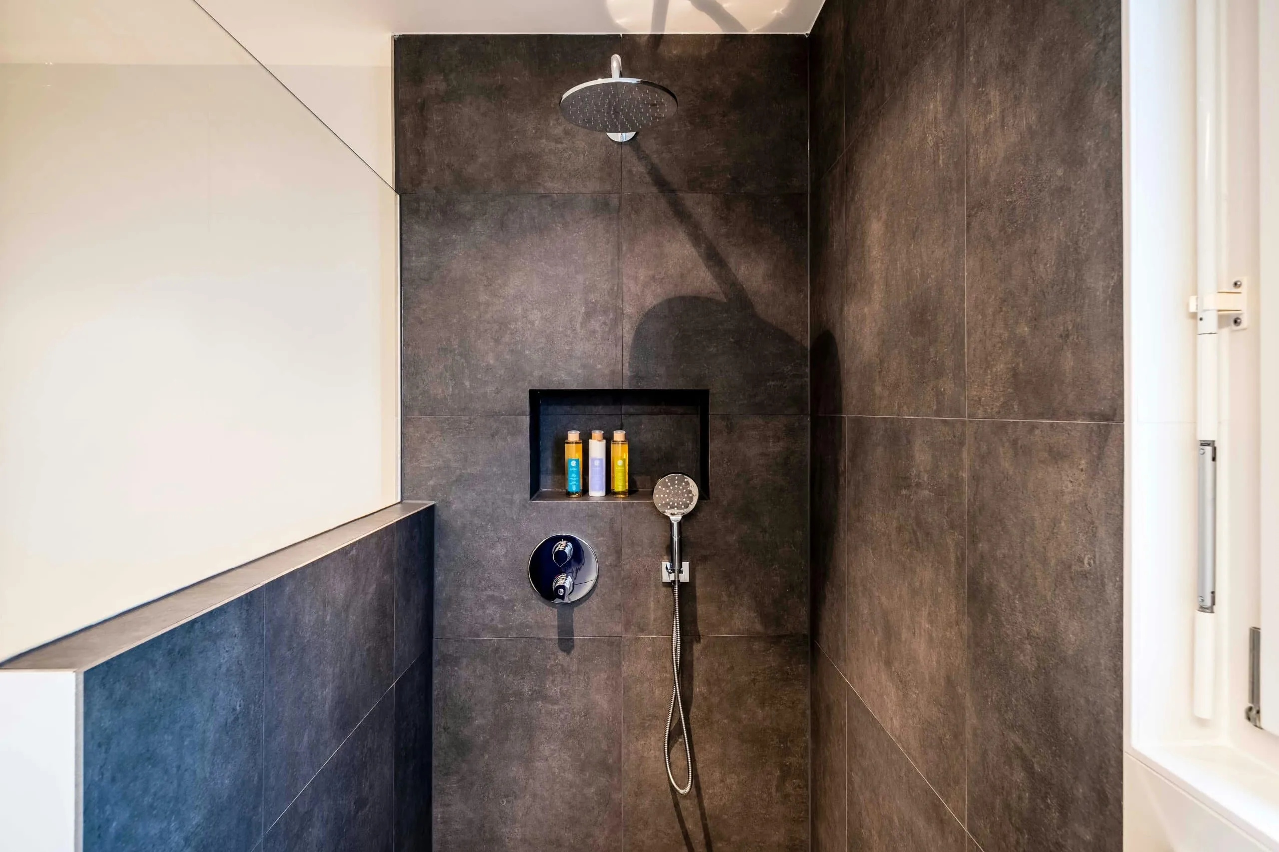 Walk-in shower with large dark gray tile walls and a lit niche