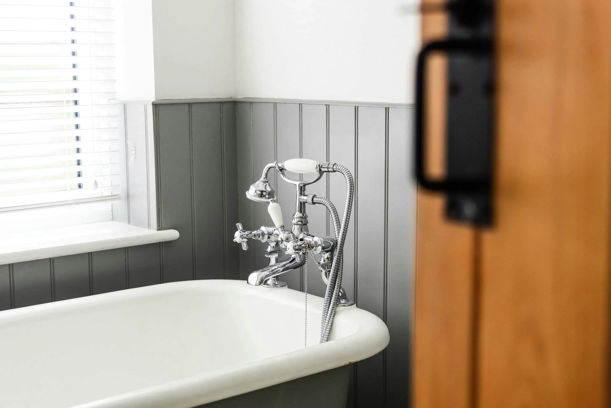 Clawfoot tub with a wall-mounted faucet beside gray paneled walls